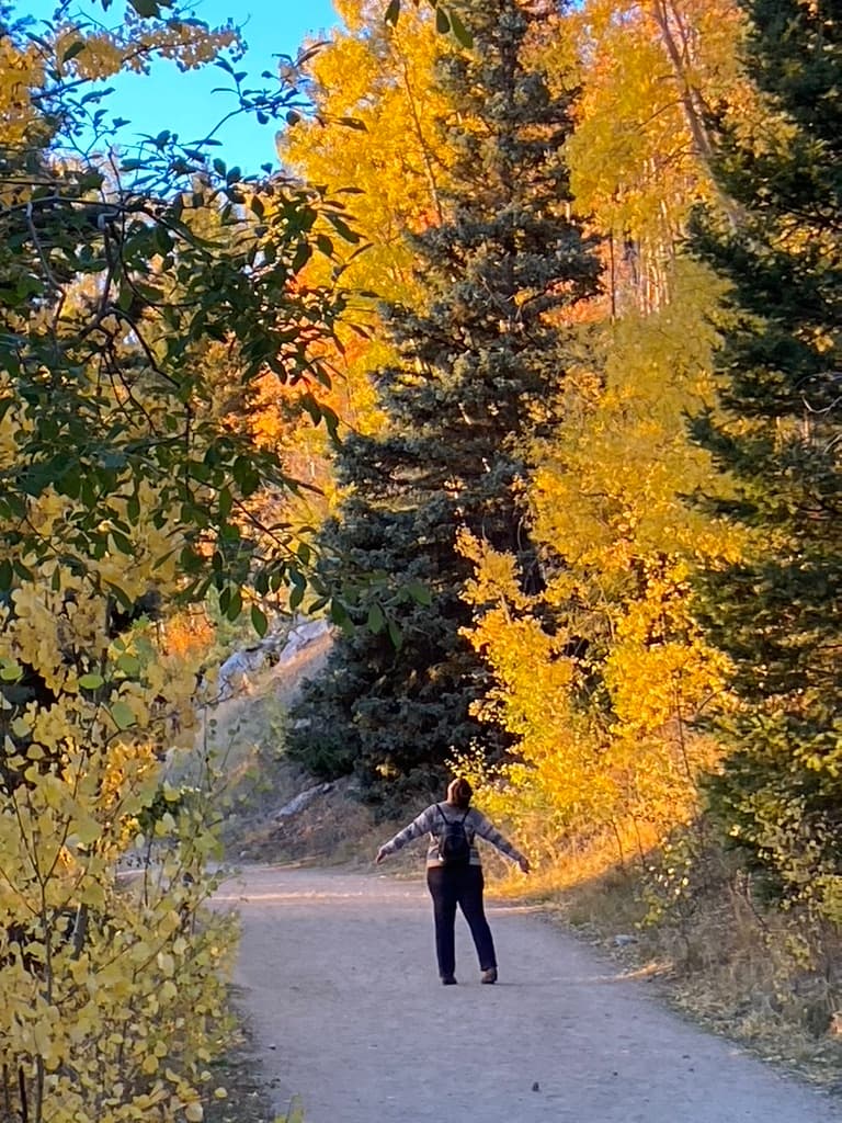 Dr. Jennifer Simon standing with her arms open on a path among aspens